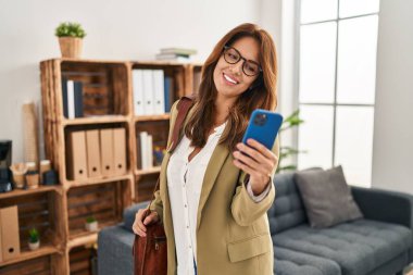 Klinikte akıllı telefon kullanan kendine güvenen genç Latin kadın.