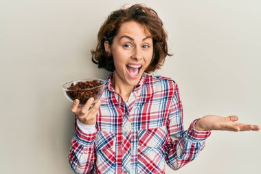 Genç esmer kadın elinde kuru üzümlerle başarıyı mutlu bir gülümsemeyle kutluyor ve kazanan el kaldırarak ifade ediyor. 