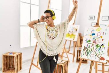 Genç İspanyol kadın sanat stüdyosunda müzik dinlerken kendinden emin bir şekilde gülümsüyor.