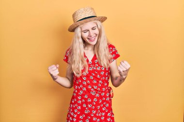 Sarışın, yaz şapkası takan güzel beyaz bir kadın. Başarı için heyecanlı. Kolları havada ve gözleri kapalı zaferi kutluyor. Kazanan konsept. 