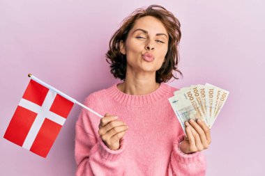 Genç esmer kadın Norveç bayrağı tutuyor ve Krone banknotları kameraya bakıyor. Öpüşme sahnesi güzel ve seksi. aşk ifadesi. 