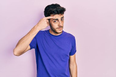 Gündelik tişört giyen genç İspanyol adam alnındaki sivilceden mutsuz olduğunu gösteriyor. Siyah noktalı çirkin bir enfeksiyon. sivilce ve deri problemi 