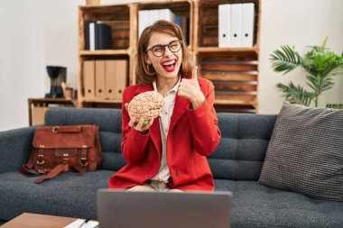 Muayenehanedeki genç esmer kadının beyni mutlu ve olumlu gülümsüyor, başparmağı mükemmel ve onay işareti yapıyor. 