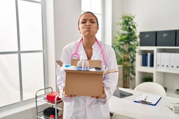 Young Hispanic Doctor Holding Box Medical Items Puffing Cheeks Funny — Stock Photo, Image