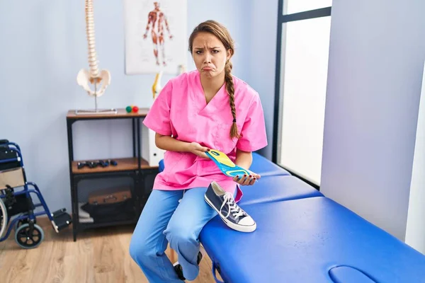 Fizyoterapi kliniğinde ayakkabı tabanı tutan genç İspanyol kadın depresyonda ve endişe içinde, kızgın ve korkmuş bir şekilde ağlıyor. hüzünlü ifade. 