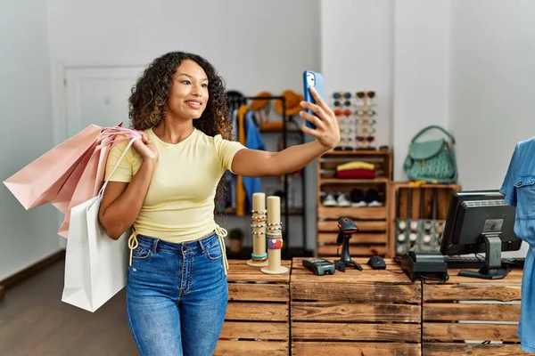 Genç Latin müşteri kadın alışveriş torbaları tutuyor ve elbise mağazasında akıllı telefon ile selfie çekiyor..