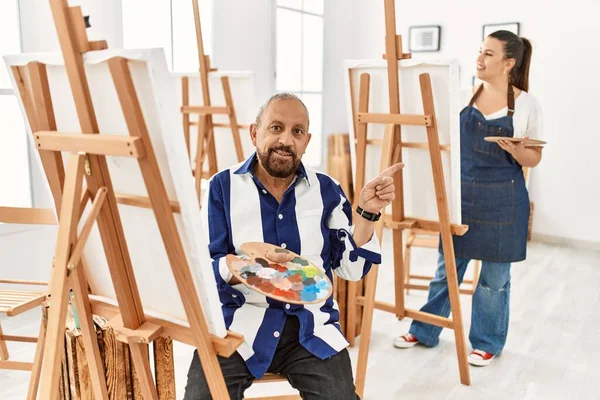 Sanat stüdyosundaki kıdemli sanatçı yüzünde kocaman bir gülümsemeyle kameraya el ile işaret ederek bakıyor.. 