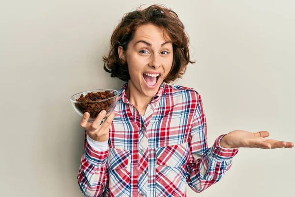 Genç esmer kadın elinde kuru üzümlerle başarıyı mutlu bir gülümsemeyle kutluyor ve kazanan el kaldırarak ifade ediyor. 