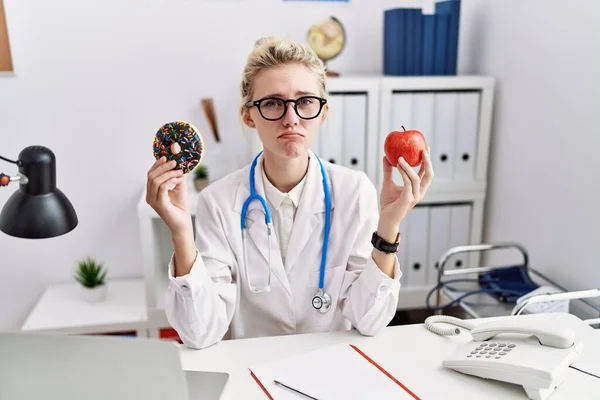 Young Doctor Woman Holding Red Apple Donut Clinic Depressed Worry — Foto de Stock