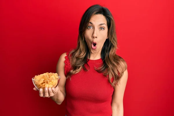 Young Latin Woman Holding Potato Chip Scared Amazed Open Mouth — Stock Photo, Image