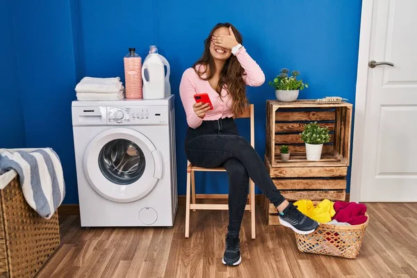 Mujer Hispana Joven Sentada Esperando Lavandería Usando Teléfono Inteligente Sonriendo —  Fotos de Stock