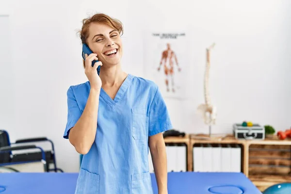 Νεαρή Καυκάσια Φυσιοθεραπεύτρια Χαμογελά Ευτυχισμένη Μιλώντας Στο Smartphone Της Κλινικής — Φωτογραφία Αρχείου
