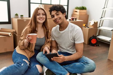 Genç çift mutlu bir şekilde dokunmatik ped kullanıyor ve yeni evlerinde kahve içiyor..