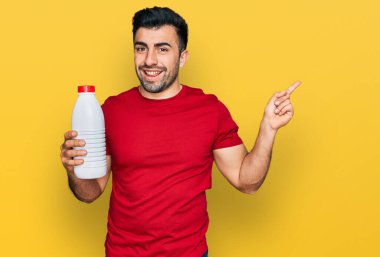 Sakallı İspanyol adam, elinde litre süt şişesi, gülümsüyor, mutlu bir şekilde elini ve parmağını kenarı gösteriyor. 