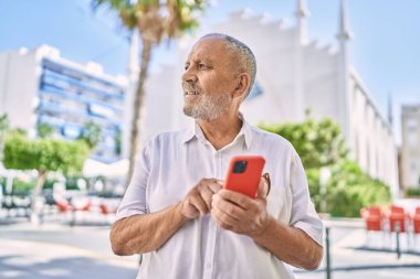 Kıdemli adam sokakta akıllı telefon kullanarak kendinden emin gülümsüyor.