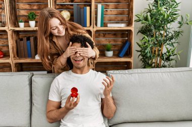 Mutlu gülümseyen genç çift ellerinde nişan yüzüğüyle kanepede oturuyor..