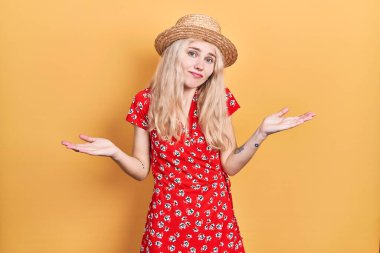 Sarı saçlı, yaz şapkası takan, kafası karışık, kolları ve elleri havada güzel beyaz bir kadın. şüphe kavramı. 