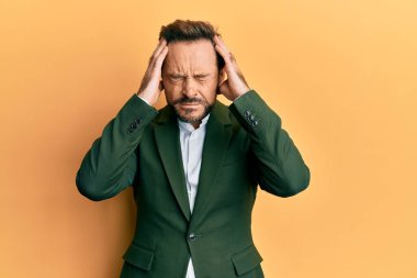 Orta yaşlı bir adam iş elbisesi giyiyor. Ağrı ve migren yüzünden baş ağrısı ve stresten muzdarip. Eller başının üstünde.. 