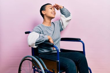 Tekerlekli sandalyede oturan çok mutlu ve gülümseyen kısa saçlı güzel İspanyol kadın başıyla uzaklara bakıyor. arama kavramı. 