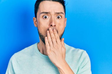 Latin asıllı genç adam gündelik giysiler giyip ağızlarını eliyle kapatıyor, şok geçiriyor ve hata yapmaktan korkuyor. şaşırmış ifade 