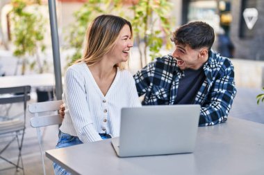 Genç bir adam ve bir kadın kahve dükkanının terasında video görüşmesi yapıyorlar.