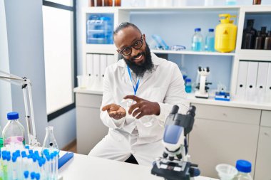 Genç Afrikalı Amerikalı adam laboratuarda dezenfektan jeli kullanan bilim adamı üniforması giyiyor.