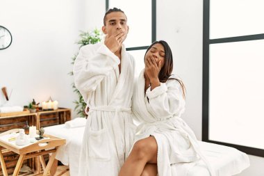 Güzellik merkezinde havluyla dikilen genç latin çift ağızlarını eliyle kapatmaktan sıkılmış. Huzursuz ve uykulu.. 