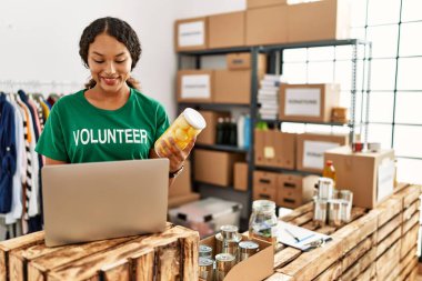 Genç Latin kadın gönüllü üniforması giyiyor hayır kurumunda dizüstü bilgisayar kullanıyor.