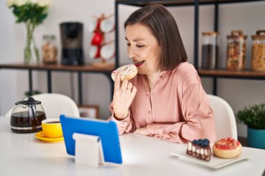 Orta yaşlı kadın kahvaltısını yapıyor. Evde masada oturuyor.