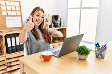 Ofiste çalışan genç esmer kadın dizüstü bilgisayarla el hareketlerini onaylıyor, gülümsüyor ve başarı için seviniyor. kazanan jest. 