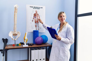 Fizyoterapi kliniğindeki anatomi raporunu gösteren fizyoterpist üniforma giyen genç sarışın kadın.