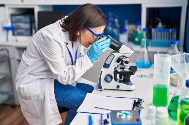 Laboratuvarda mikroskop kullanarak gülümseyen orta yaşlı bilim kadını.