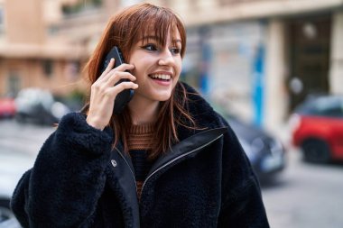 Gülümseyen genç bir kadın caddedeki akıllı telefondan konuşuyor.