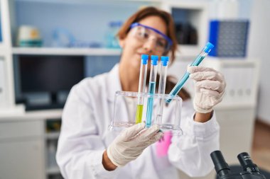 Laboratuvarda test tüpleri tutan bilim adamı üniforması giyen genç Latin bir kadın.