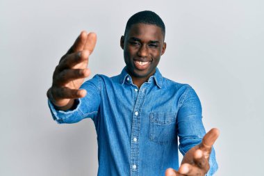 Gündelik giysiler giymiş genç Afro-Amerikan bir adam kameraya sarılıp gülümseyerek bakıyor. Mutluluğu kucaklayan neşeli bir ifade.. 