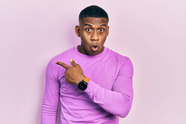 Gündelik pembe süveter giyen genç siyah adam parmaklarını yana doğru göstererek şaşırdı, ağzı açık hayret içinde kaldı.. 