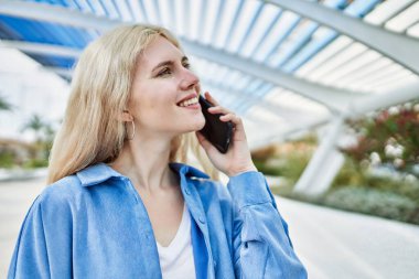 Genç sarışın kadın güneşli bir günde telefonda konuşuyor.