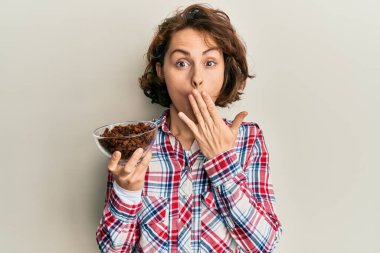 Genç esmer kadın elinde kuru üzümlü bir kâse, ağzı elle kapatılmış, şok olmuş ve hata yapmaktan korkan. şaşırmış ifade 