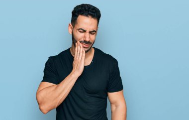 Sakallı, sıradan siyah tişörtlü İspanyol bir adam diş ağrısı ya da diş ağrısı yüzünden ağzıyla dokunuyor. dişçi 