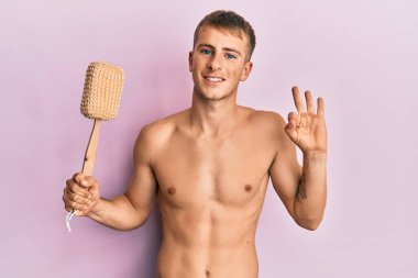 Beyaz, üstsüz, duş süngeri tutan genç adam parmaklarıyla imza atıyor, gülümseyerek mükemmel bir sembol oluşturuyor. 