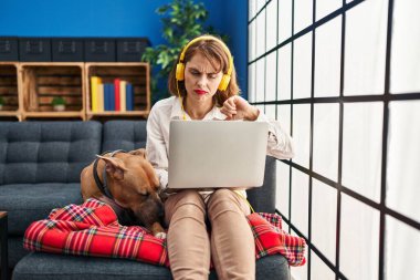 Genç ve güzel bir kadın dizüstü bilgisayarını kızgın yüzüyle koltukta oturuyor. Eksi işareti baş parmakları aşağıda, reddedilme konsepti ise reddedilmiş. 