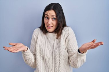 Genç esmer kadın mavi arka planda duruyor. Neşeli gülümsüyor ve kollarını açıyor. Dostça karşılama, olumlu ve kendinden emin selamlar. 