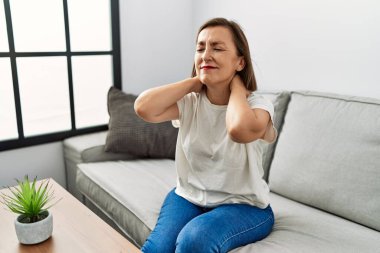 Orta yaşlı İspanyol bir kadın evinde boynu ağrıyan bir kanepede oturuyor.