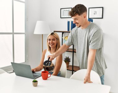 Kadın evde dizüstü bilgisayar kullanıyor ve erkek arkadaşı kahve dolduruyor..