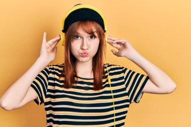 Kızıl saçlı, müzik dinleyen, kulaklık takan komik yüzlü genç bir kadın. Ağzı havayla şişer, havayı yakalar.. 