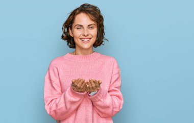 Elleri avuçlarında gülümseyen ya da el hareketi yapan gündelik kıyafetler giyen İspanyol genç bir kadın. Bekleme ve koruma 