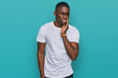 Sıradan beyaz tişörtler giyen genç Afro-Amerikan bir adam diş ağrısı ya da diş hastalığından dolayı ağızlarına acı dolu bir ifadeyle dokunuyor. dişçi 