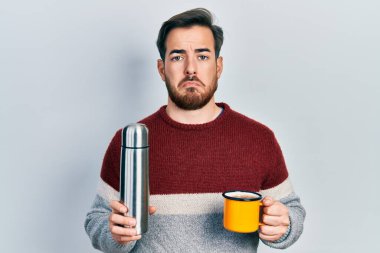 Sakallı, elinde termometreyle kahve içen yakışıklı beyaz bir adam. Depresyonda ve üzüntüden ağlıyor, ağlıyor ve korkuyor. hüzünlü ifade. 