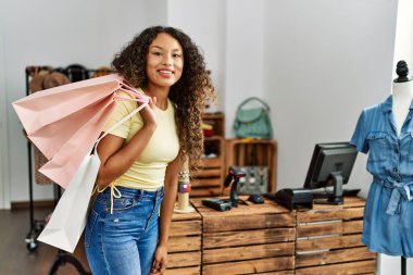 Genç Latin müşteri gülümseyen kadın giyim mağazasında alışveriş torbalarını tutarken mutlu..