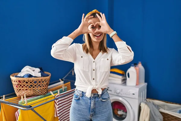 Young Blonde Woman Laundry Room Doing Heart Shape Hand Fingers — Stock Photo, Image